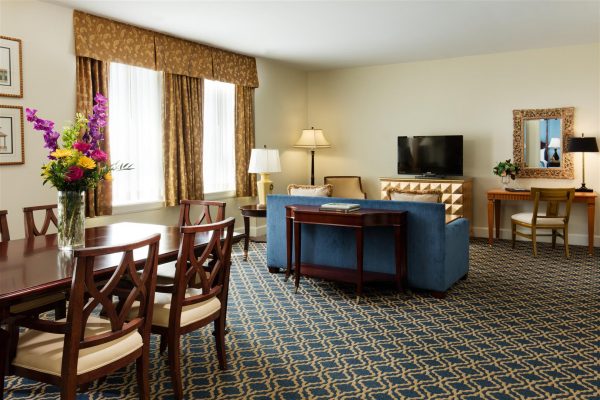 A suite is show featuring the living and dining room space. Blue and gold accents are throughout the space.