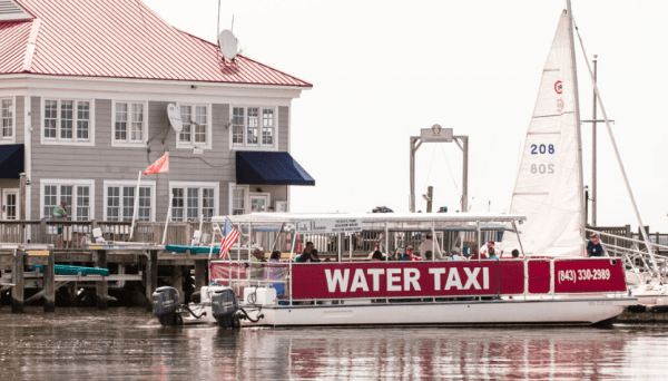A boat that is called a water taxis cruises on the water and a large grey building is in the background.