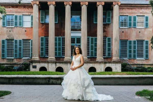 A bride stands in front of a building with green shutters.