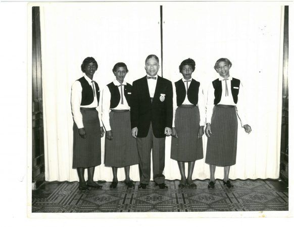 Four women stand in a row with a man standing in between them in the middle.